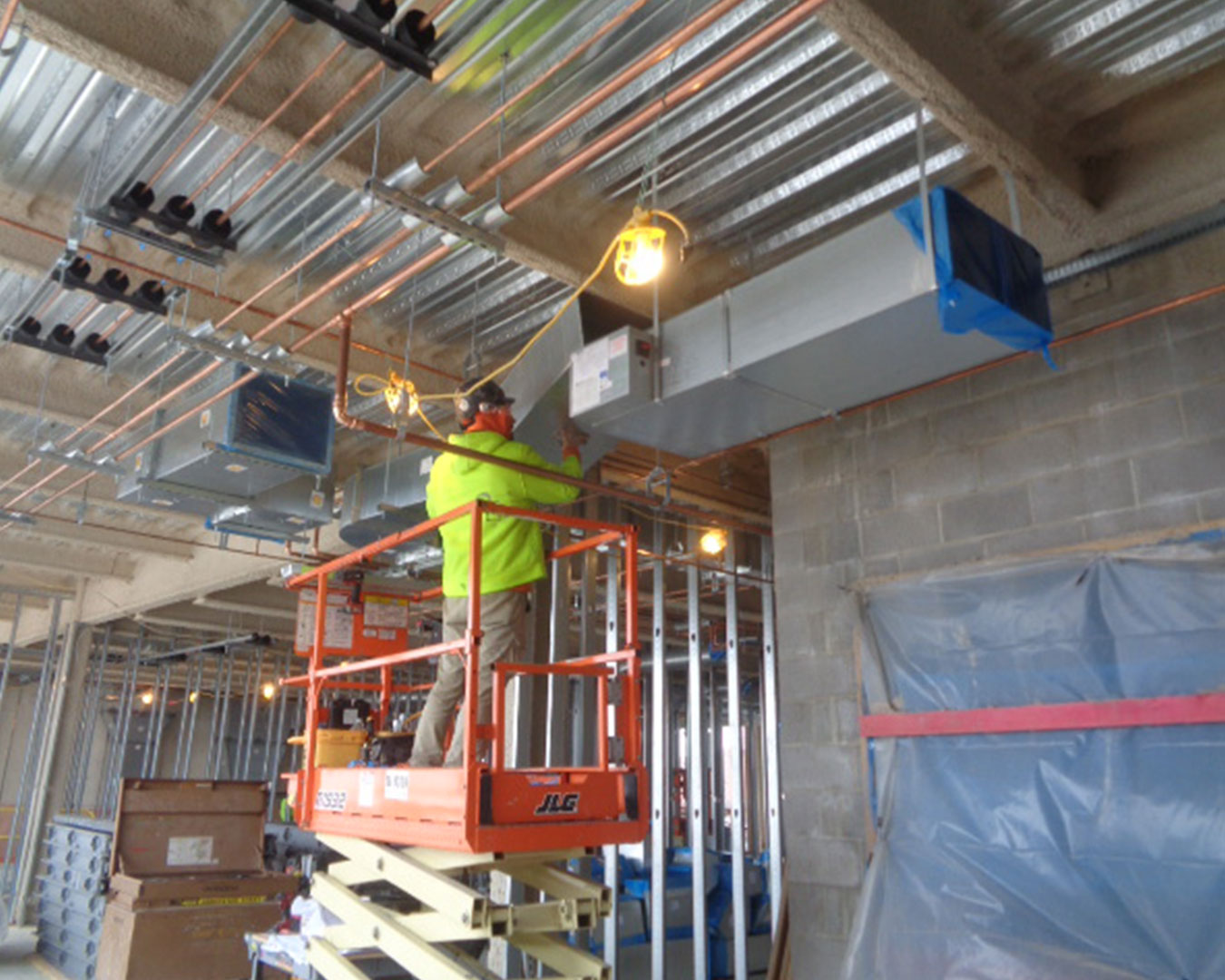 worker on a hydraulic lift installing ventilation duct