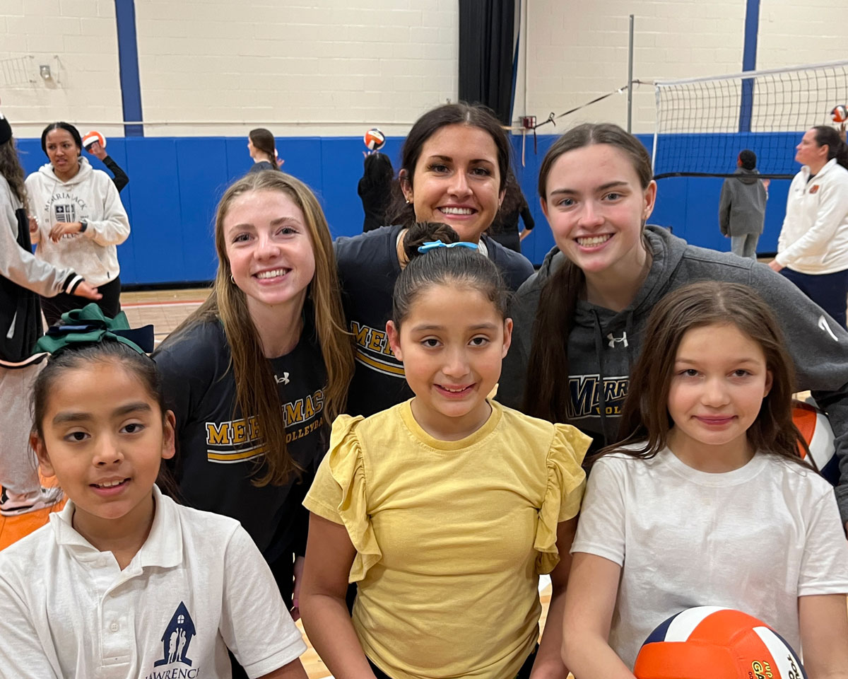 Vrouwelijke Lawrence-studenten poseren met volleybal met vrouwelijke volleybalspelers van Merrimack College