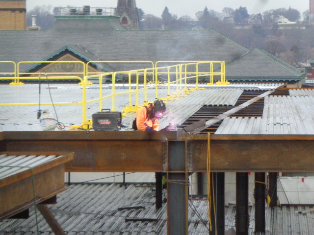 građevinski radnici koji zavaruju metalni rub na konstrukcijsku gredu